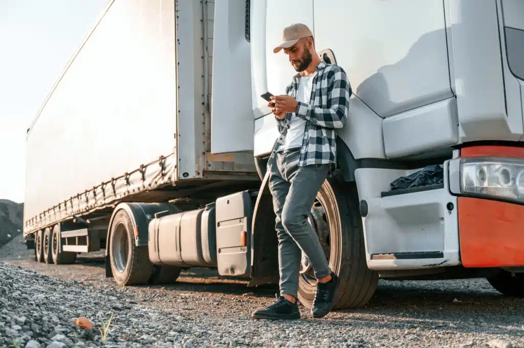 Trucking Name Ideas. Truck driver standing next to his truck searching on his phone.